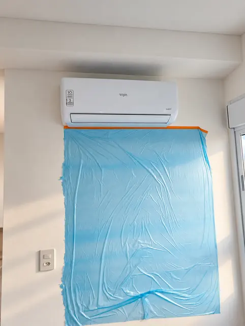 Parede protegida com lona azul abaixo do split durante o serviço